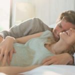 Affectionate pregnant couple laying in bed laughing
