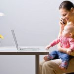 Working mother holding baby while talking on cell phone at desk
