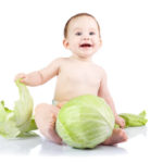 Beautiful little baby on a white background with green cabbage.